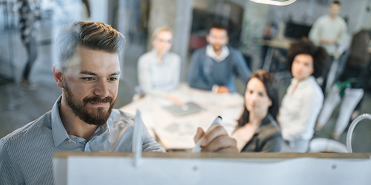 Mann steht während Workshop an Whiteboard, dahinter weitere Teammitglieder